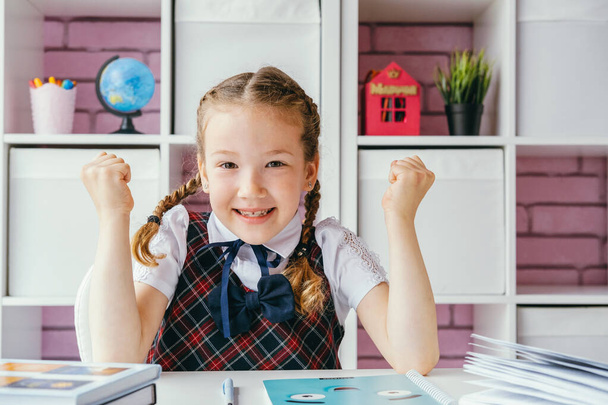 Beautiful little schoolgirl wearing  school uniform,sitting at the desk and enjoying back to school. - Foto, immagini