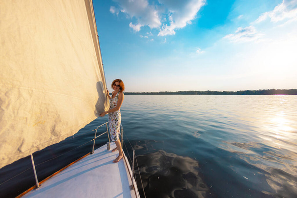 ヨットで旅を。少女は船の弓の上に立って距離を調べる。白いヨットのデッキで休んで. - 写真・画像
