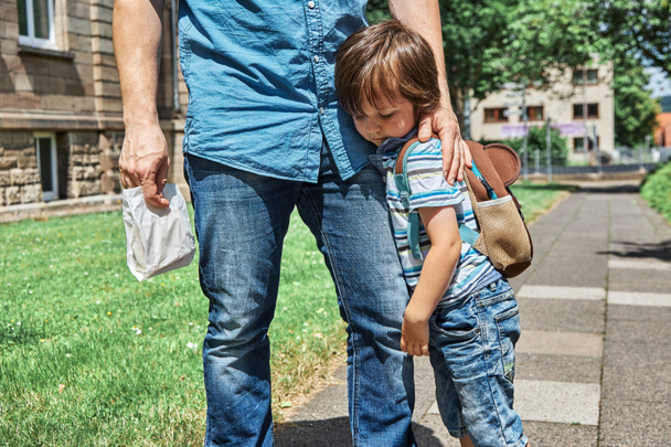 Malý chlapec objímá svého otce za nohu před školou nebo školkou. Childs strach, nejistota, rozpaky a rodičovská podpora v těžkých časech - Fotografie, Obrázek