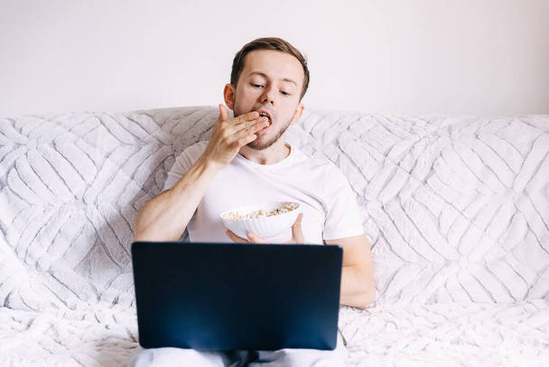 Young man watch tv on laptop in his own apartment. Happy positive male person have fun and pleasure Alone in room - 写真・画像