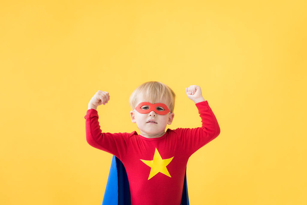 Portrait of superhero child. Super hero kid against yellow paper background. Happy child wearing red mask and cape of superhero. Children dream and imagination concept - Photo, Image