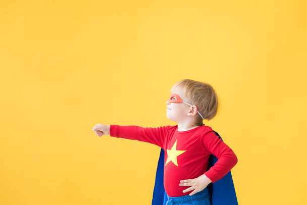 Portrait of superhero child. Super hero kid against yellow paper background. Happy child wearing red mask and cape of superhero. Children dream and imagination concept - Foto, Bild