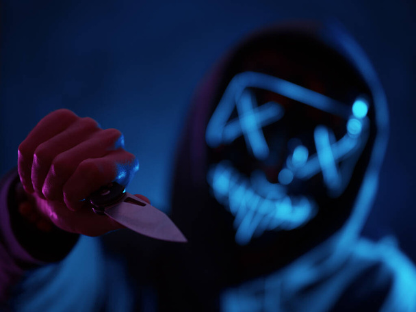 Halloween is een griezelig beeld van een moordlustige maniak in een gloeiend masker met een mes. Neon Portret - Foto, afbeelding