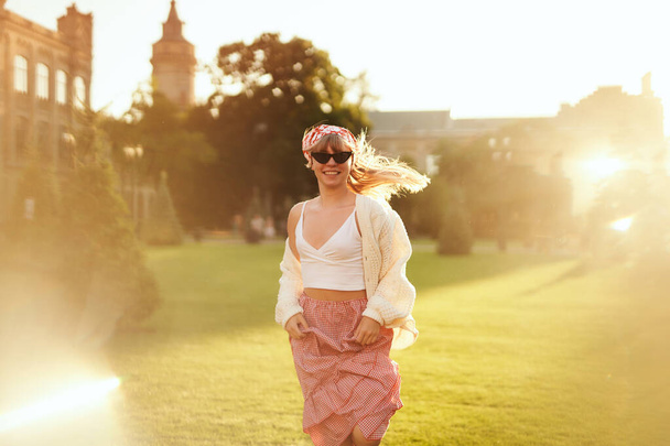Kobieta w sukience, chustce i swetrze biegnie po parku o zachodzie słońca - Zdjęcie, obraz