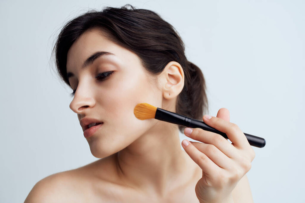 mujer con hombros desnudos aplicar maquillaje en la cara cepillo de maquillaje - Foto, imagen