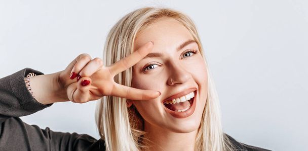 Hey smile you. Portrait of cheeky and cute glamor blond woman combed hair and jacket winking happily showing peace victory gesture as fooling around, being optimistic - Photo, image