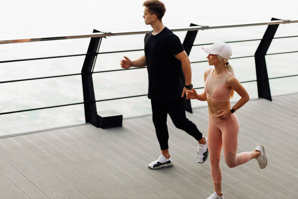 Young sportive couple in sportswear running sprint on the bridge on the coast, Fit Runner fitness runner during outdoor workout at sunrise, sports, motivation, healthy lifestyle - Φωτογραφία, εικόνα