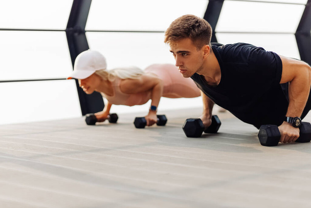 Young couple exercising outdoors, Attractive sportive woman and handsome muscular man are exercising on the bridge on the coast, Doing plank on kettlebell, doing push-ups, Sport concept, motivation - Foto, Imagem