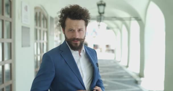 sexy smart casual guy posing outside, holding hands on jacket button and unbuttoning, opening jacket, scratching beard and thinking against city background - Кадри, відео