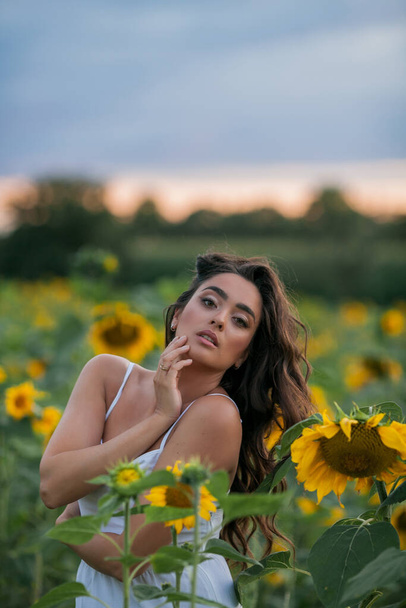 Portrait of a young beautiful woman with dark hair in a sunflower field at sunset. Happy. - Photo, Image
