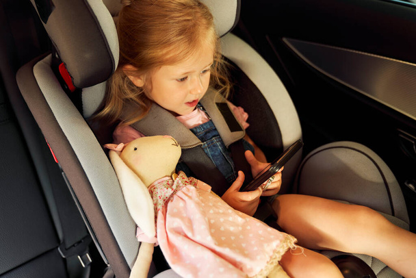 Girl sitting in the baby car seat and using phone                               - Photo, Image