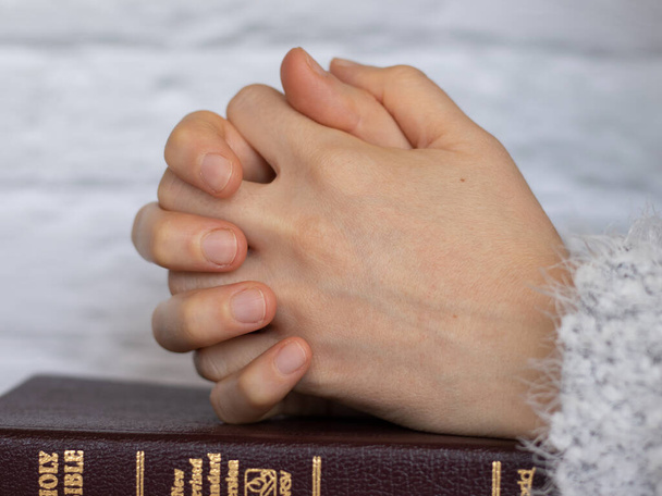 Ihmisen rukoilevat kädet rukoilevat suljetulla Pyhällä Raamatulla. Nuori nainen rukoilee Isää Jumalaa ja Herraa Jeesusta Kristusta aamulla katuvalla sydämellä. - Valokuva, kuva