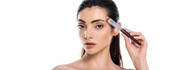 brunette woman applying face foundation with cosmetic brush isolated on white, banner - Фото, зображення