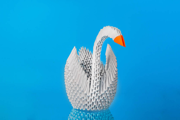 White origami swan made of paper with a red beak on a blue background. - Fotografie, Obrázek