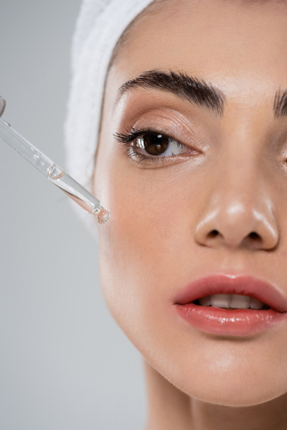 close-up van jonge vrouw aanbrengen vitamine c serum met pipet geïsoleerd op grijs - Foto, afbeelding