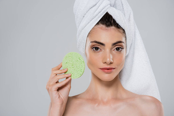 young woman with towel on head holding green beauty sponge isolated on grey  - Foto, afbeelding