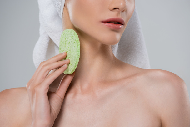 обрезанный вид молодой женщины, держащей зеленую губку красоты изолированы на серый  - Фото, изображение