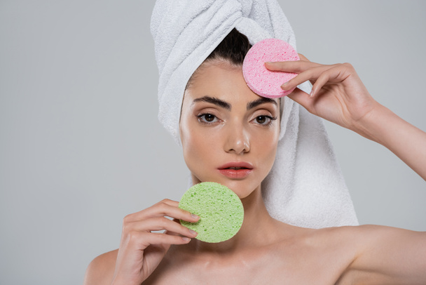 young woman with towel on head holding beauty sponges isolated on grey  - Foto, afbeelding