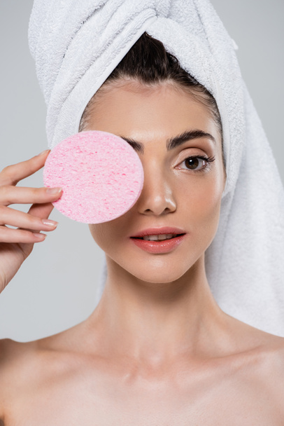 young woman with towel on head holding pink beauty sponge near eye isolated on grey  - Fotoğraf, Görsel