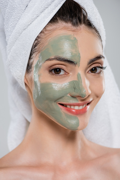 cheerful young woman with towel on head and green clay mask on face isolated on grey - Foto, Imagem