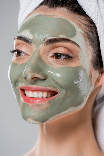 close up of positive young woman with green clay mask on face isolated on grey - Photo, image