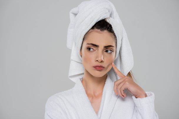 pensive young woman with towel on head pointing at cheek isolated on grey - Foto, afbeelding