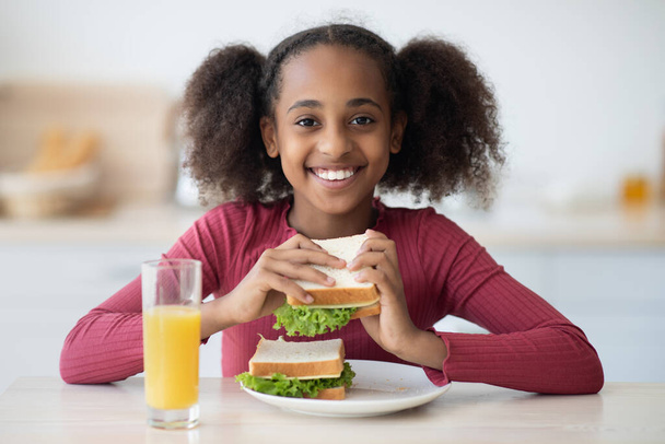 Ένα όμορφο μαύρο κορίτσι τρώει σνακ στο σπίτι. - Φωτογραφία, εικόνα