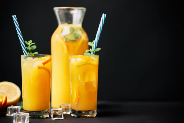 Delicious orange juice with ice, mint and fresh fruits on black table background with copy space - Zdjęcie, obraz