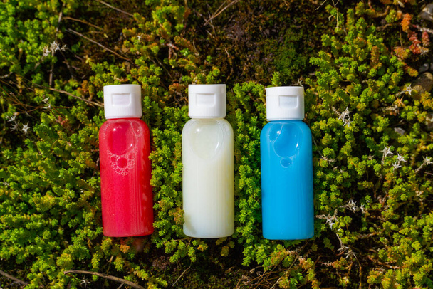 Reisekosmetik in kleinen Flaschen: Duschgel, Shampoo und Conditioner. Kosmetik in roten, blauen und weißen Farben in Gras  - Foto, Bild