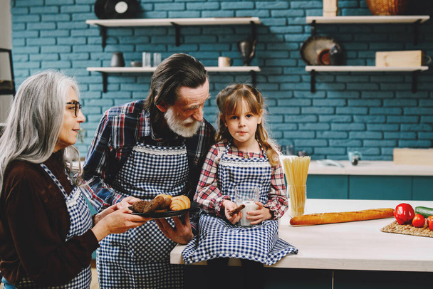 Little girl eating in the kitchen with granparents - 写真・画像