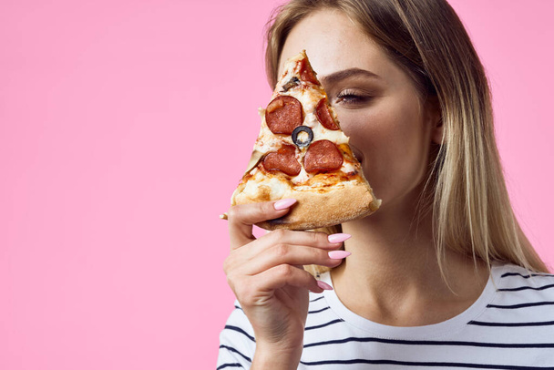 nő csíkos póló pizza a kezében gyors élelmiszer snack rózsaszín háttér - Fotó, kép