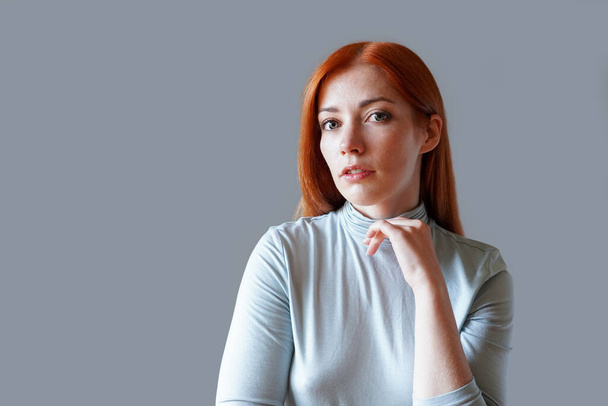 mujer joven contemplativa con el pelo rojo largo y cuello alto azul claro - Foto, imagen