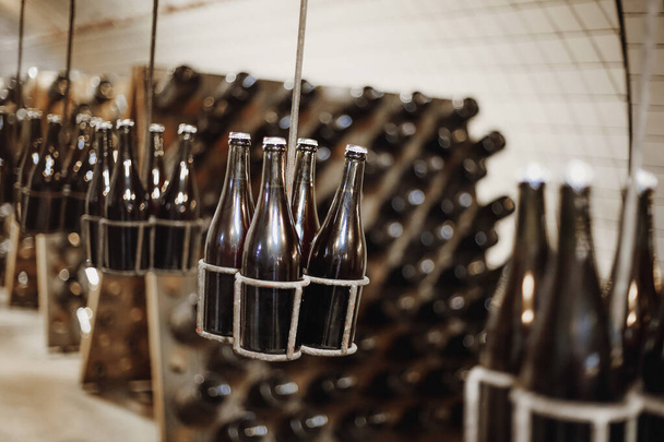 木製の倉庫や天井からぶら下がっている特別な金属ホルダーに積み上げビールやエールのボトルと地元のヴィンテージスタイルの醸造所の地下店の写真。中小企業・製造業のコンセプト - 写真・画像