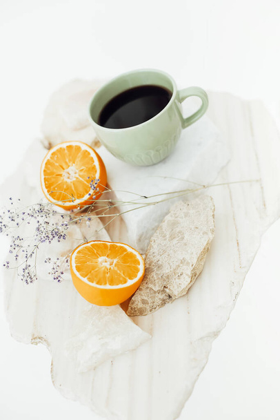 Foto de cerca desde arriba de la taza de café negro con dos mitades de naranjas cortadas en concreto y soporte de piedra con ramita de flores secas aisladas en el fondo blanco del estudio, composición creativa - Foto, Imagen