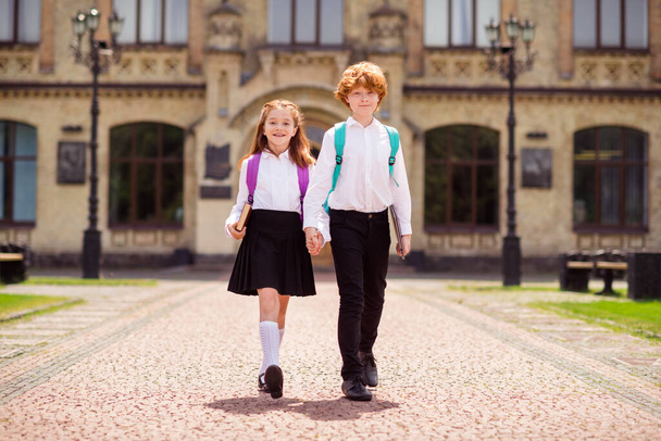 Photo of two schoolkids walk street hold hands enjoy trip wear backpack white shirt uniform park outdoors - Photo, image