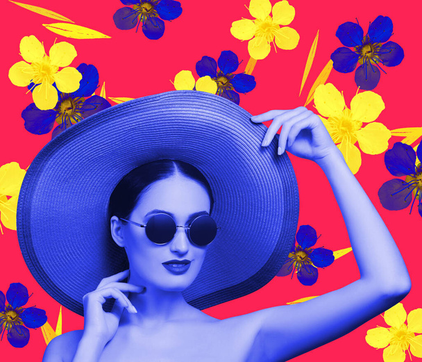 Joven modelo de moda femenina hermosa en sombrero de paja y gafas de sol sobre fondo floral azul rojo estampado de flores. Belleza, concepto de moda - Foto, Imagen