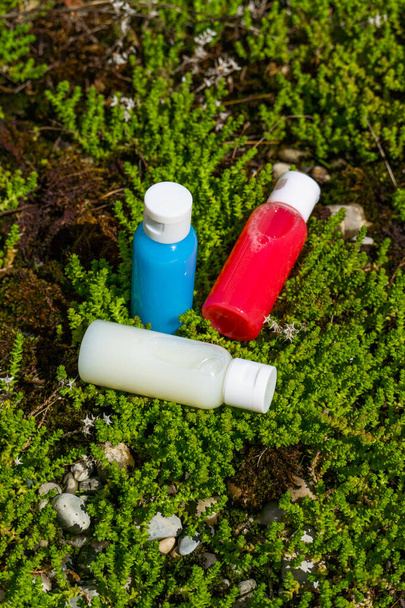 travel cosmetics in small bottles: shower gel, shampoo and conditioner. cosmetics in red, blue and white colours in gras  - Фото, изображение