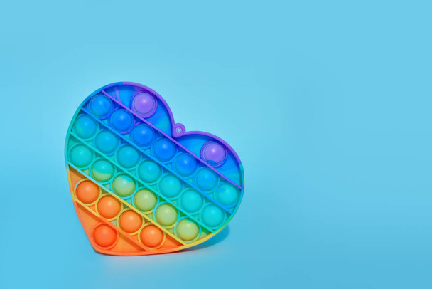 Pop it - Nuevo popular colorido silicona sensorial de moda juguete antiestrés en forma de corazón sobre un fondo azul. Arco iris color.Copiar el espacio. - Foto, imagen