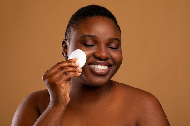 Portrait of happy black woman cleaning skin by cotton pad - Фото, зображення