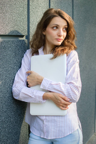 Kobieta portret młodej kobiety ze srebrnym laptopem, businesswoman jest pozowanie z tabletem cyfrowym na zewnątrz na tle ciemnej ściany czekając na spotkanie podczas przerwy od pracy - Zdjęcie, obraz