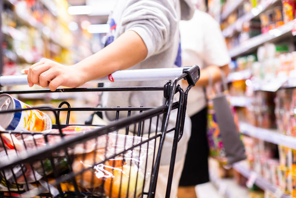 顧客の手に選択的な焦点は、スーパーマーケットでショッピングカートを押している. - 写真・画像