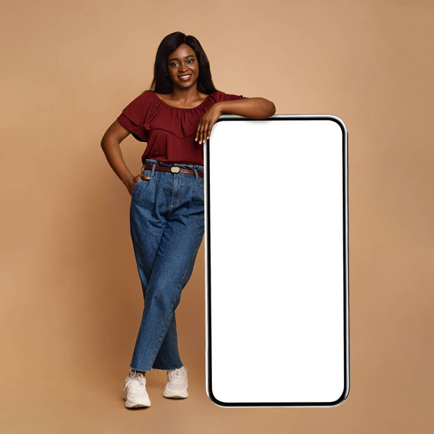 Красивая черная женщина стоит у огромного смартфона с пустым экраном - Фото, изображение