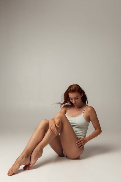 Portrait of young beautiful slim tanned red headed woman in lingerie posing isolated over gray studio background. Natural beauty concept. - Foto, immagini