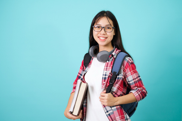 幸せな学生。陽気なアジアの女の子は青の背景にスタジオでバックパックで立ってカメラに笑みを浮かべて.学校のコンセプトに戻る. - 写真・画像