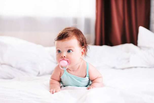een pasgeboren baby met een fopspeen in zijn handen ligt op een sneeuwwit bed. - Foto, afbeelding