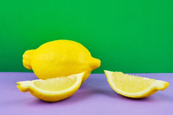 Свежие лимонные фрукты и ломтик на фиолетовом и зеленом фоне - Фото, изображение