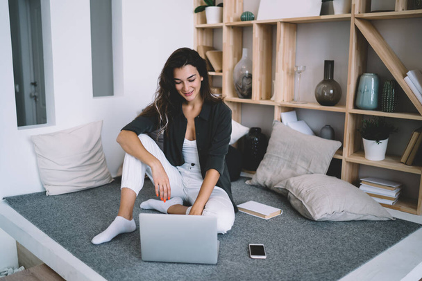 Cheerful brunette hipster girl millennial enjoying free time movie on laptop computer sitting at modern interior, positive woman freelancer enjoying remote job and wireless connection for publication - Foto, Bild