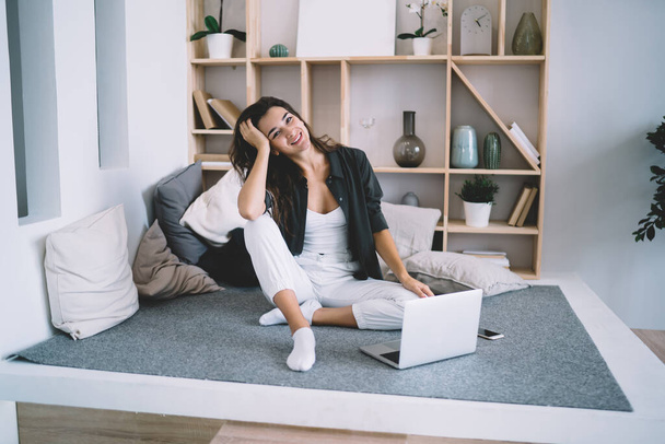 Beautiful caucasian female freelancer looking at camera working remotely at home interior enjoying wireless connection, smiling hipster girl at modern designed apartment using laptop computer for job - Foto, imagen