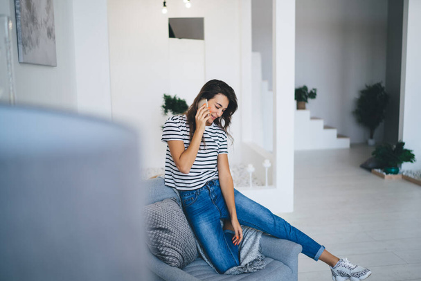 Smiling beautiful caucasian female talking on mobile phone spending time in home interior making call, cheerful woman having conversation on smartphone resting on leisure at modern apartment - Foto, Imagem