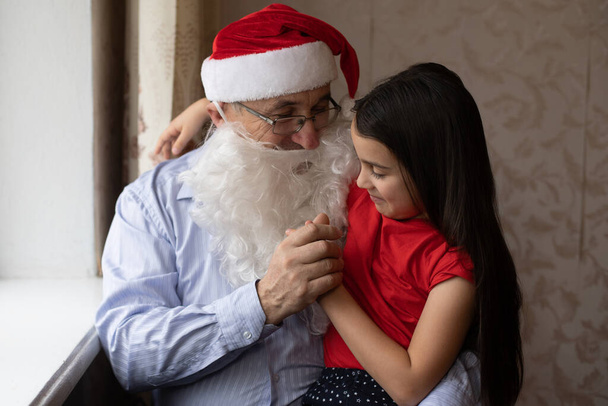 Зворотний портрет радісної дівчинки, яка обіймає дідуся в головних уборах. дідусь і внучка у капелюхах Санта - Клауса. - Фото, зображення